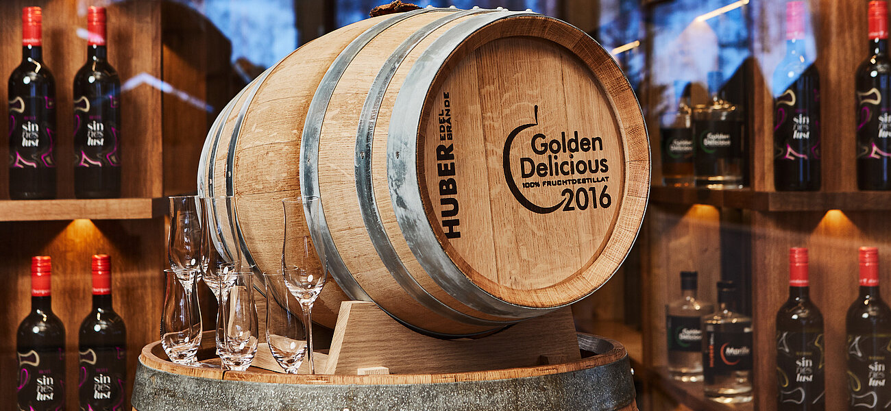 Holzfass mit Aufschrift Golden Delicious 2016 im Spirituosengeschäft mit Flaschen und Gläsern
